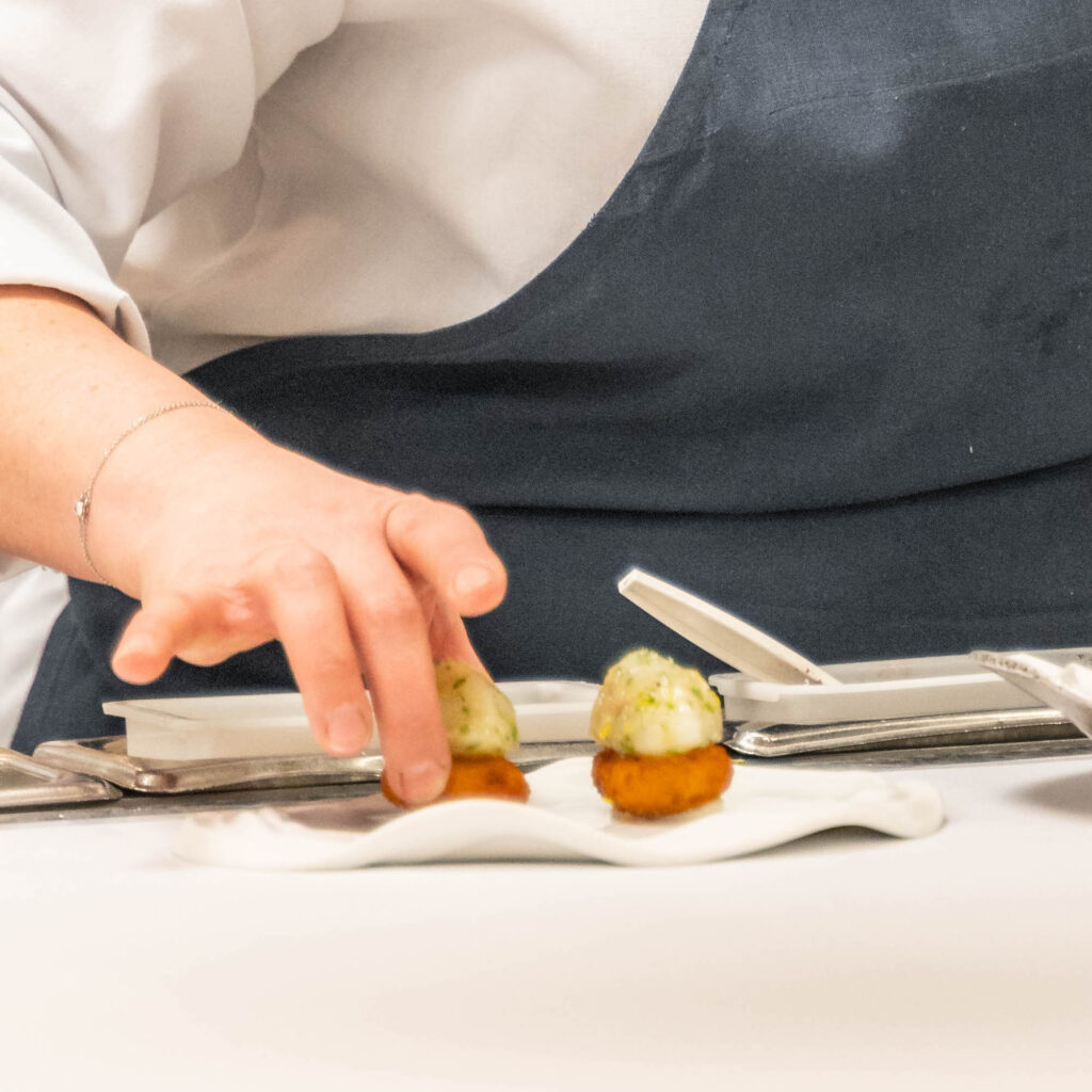 a chef's hand arranges food on a plate