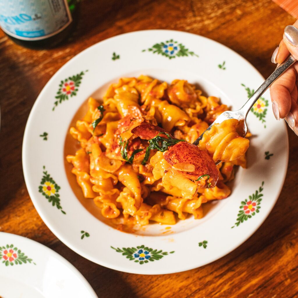 a hand holding a fork, grabbing a bite of fresh, handmade pasta and lobster at osteria morini