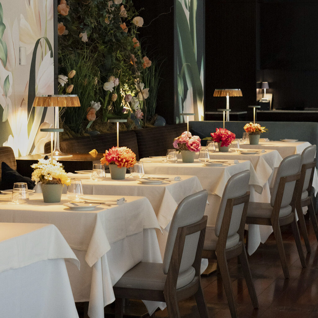 the main dining room of ai fiori at the langham new york on fifth ave - flower topped white tablecloth covered tables line a floral wall installation