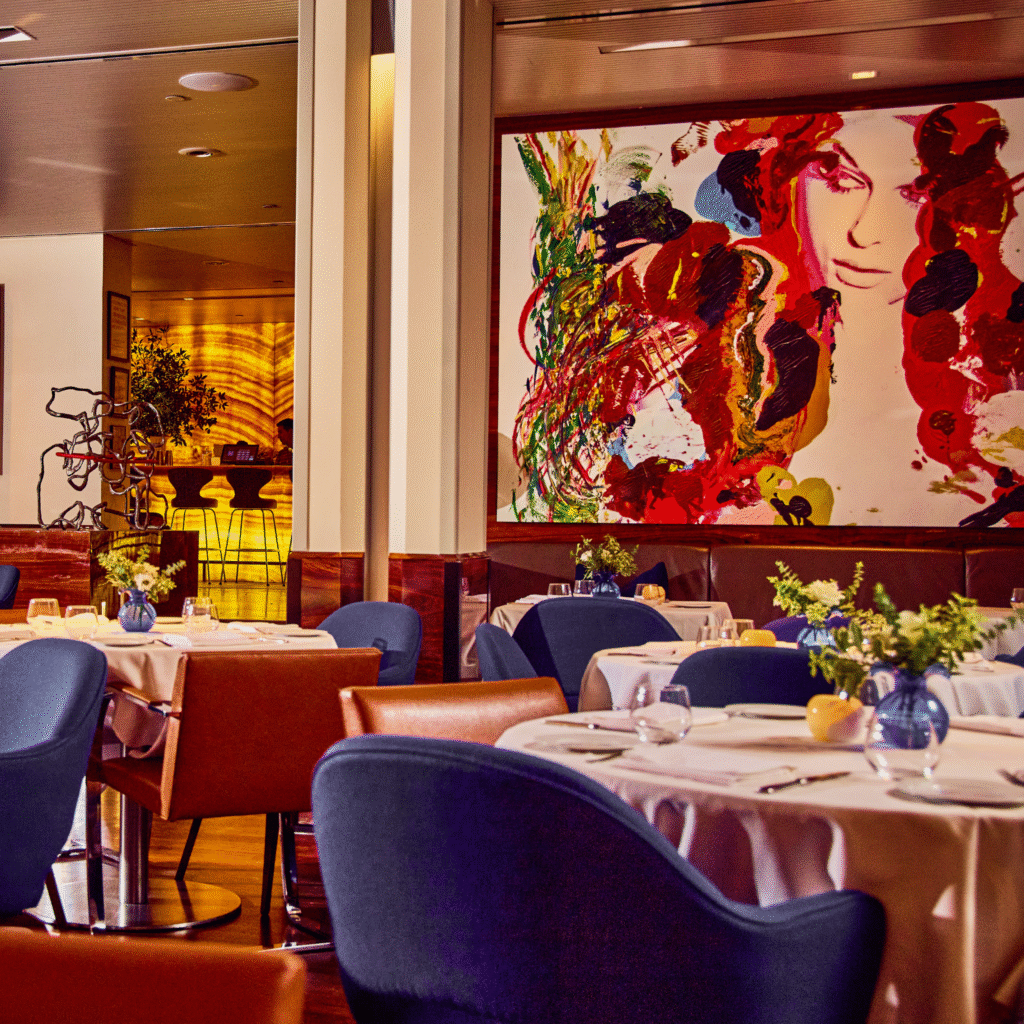 main dining room at marea new york - showcasing a bright, poppy piece of art, elegant tables, and comfortable blue chairs